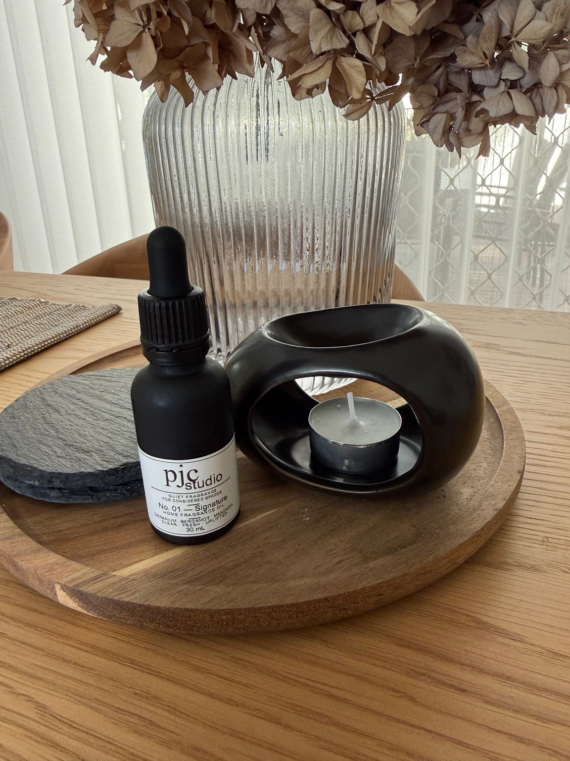 The actual matte black No. 01 oil burner and 30ml home fragrance oil styled on a wooden tray; decorative tray, vase and coasters are not included.